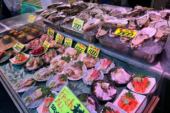 Fish and shellfish on ice at a Tsukiji stall, each tray under a green price tag
