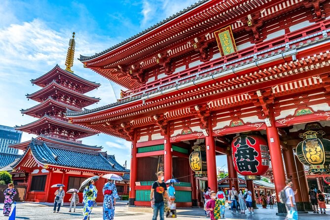 The red main gate and five-storey pagoda of Senso-ji in Asakusa, with visitors crossing the forecourt under a blue sky